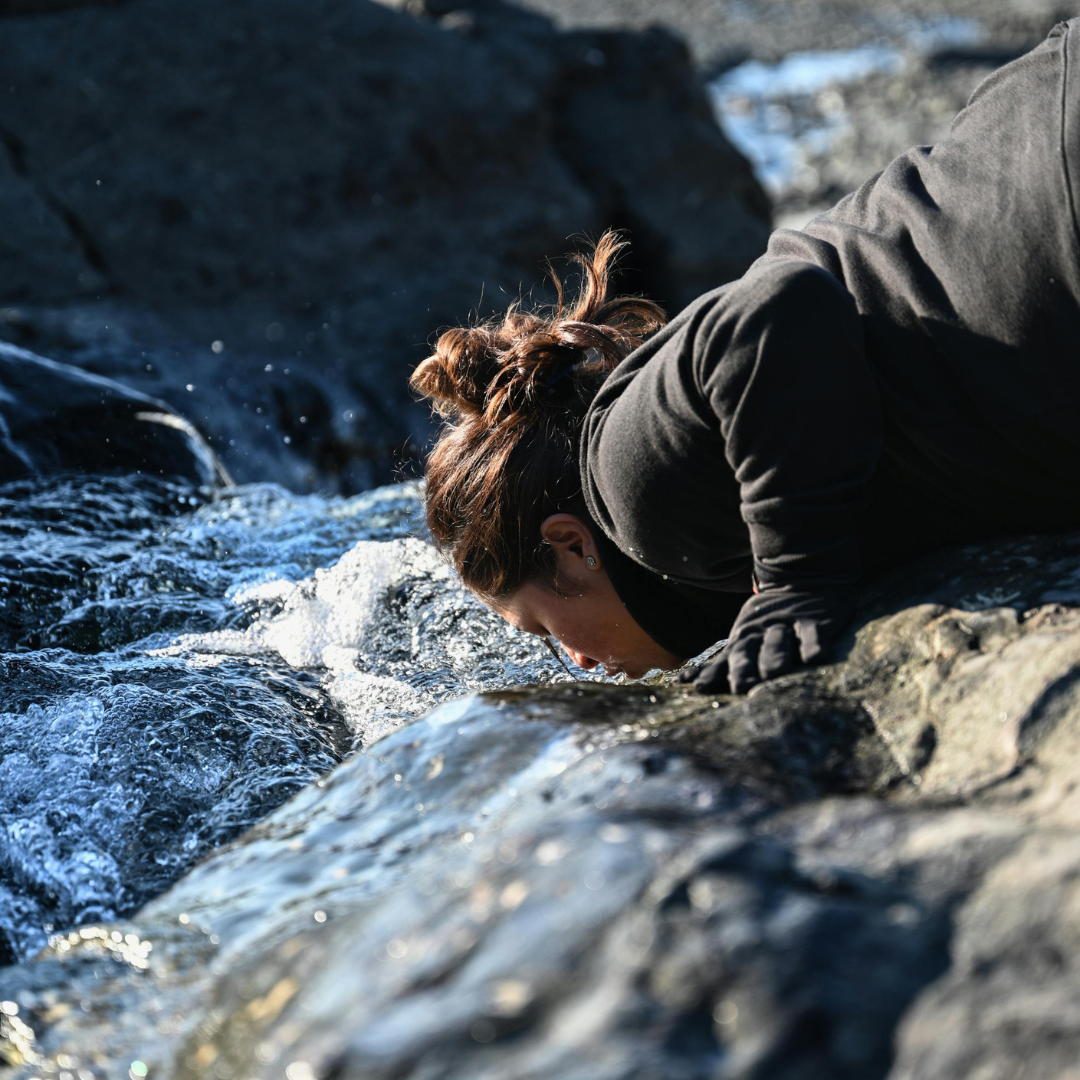 Woman drinking water from mountain stream while hiking outdoors